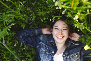 Cheerful teenage girl lying on grass in park - IHF00898