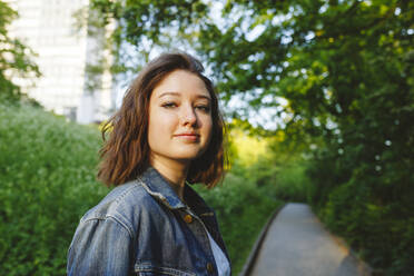 Girl in denim jacket standing at public park - IHF00900