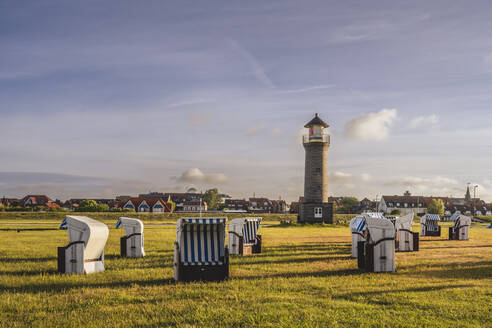 Germany, Lower Saxony, Juist, Hooded beach chairs in front of Memmertfeuer lighthouse - KEBF02309