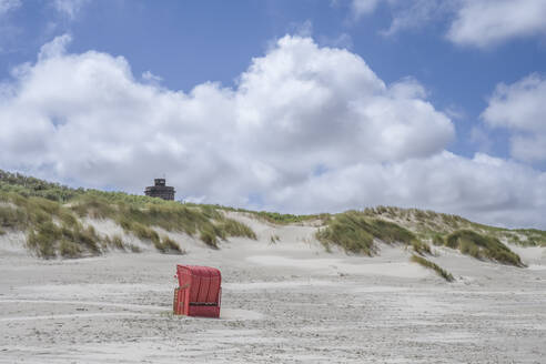 Deutschland, Niedersachsen, Juist, Strandkorb mit Kapuze am leeren Strand mit Dünen im Hintergrund - KEBF02316