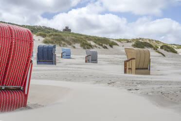 Deutschland, Niedersachsen, Juist, Strandkörbe mit Kapuze am leeren Strand mit Dünen im Hintergrund - KEBF02317