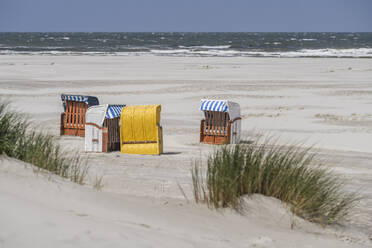 Deutschland, Niedersachsen, Juist, Strandkörbe mit Kapuze am leeren Strand mit klarer Linie des Horizonts über der Nordsee im Hintergrund - KEBF02321