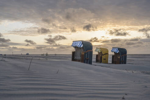 Deutschland, Niedersachsen, Juist, Strandkörbe mit Kapuze am leeren Strand bei Sonnenuntergang - KEBF02328