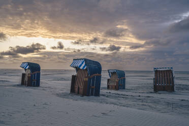 Deutschland, Niedersachsen, Juist, Strandkörbe mit Kapuze am leeren Strand bei Sonnenuntergang - KEBF02329