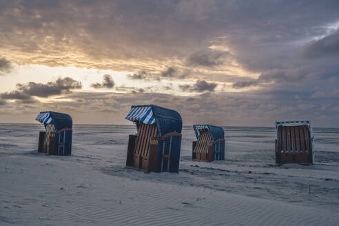 Deutschland, Niedersachsen, Juist, Strandkörbe mit Kapuze am leeren Strand bei Sonnenuntergang - KEBF02329