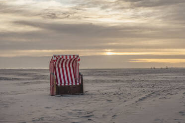 Deutschland, Niedersachsen, Juist, Strandkorb mit Kapuze am leeren Strand bei Sonnenuntergang - KEBF02336