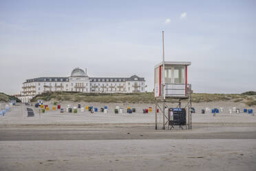 Deutschland, Niedersachsen, Juist, Rettungsschwimmerhütte und vermummte Strandkörbe am leeren Strand mit Strandhotel Kurhaus im Hintergrund - KEBF02337