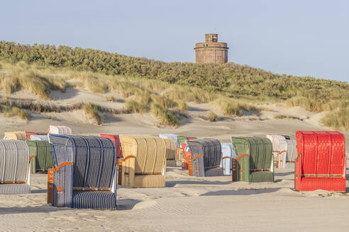 Deutschland, Niedersachsen, Juist, Strandkörbe mit Kapuze am leeren Strand mit Wasserturm im Hintergrund - KEBF02341