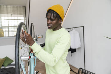 Young man repairing wheel of bicycle at home - VPIF06435