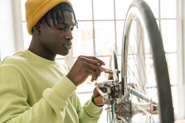 Young man repairing bicycle chain at home - VPIF06438