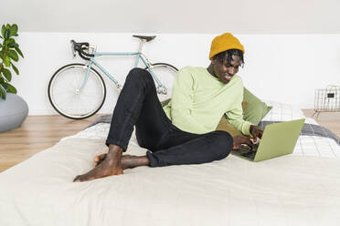 Smiling businessman working on laptop in bedroom - VPIF06452