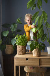 Girl with spray bottle watering potted plants at home - SVKF00280