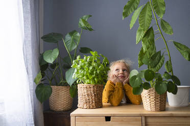 Contemplative girl by houseplants on table at home - SVKF00282