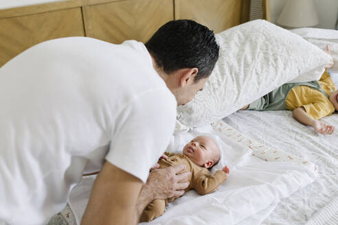 Lächelnder Mann spielt mit Baby auf dem Bett zu Hause - TYF00223