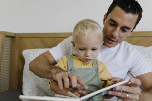 Vater liest ein Buch mit seinem Sohn, der zu Hause auf dem Bett sitzt - TYF00228