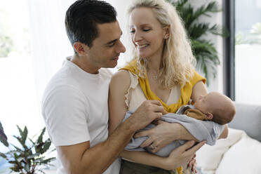 Smiling woman carrying baby in arm sitting by man at home - TYF00249