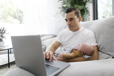 Mann mit Baby auf dem Arm arbeitet von zu Hause aus - TYF00255