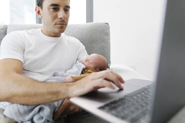 Mann mit Baby auf dem Arm arbeitet von zu Hause aus - TYF00256