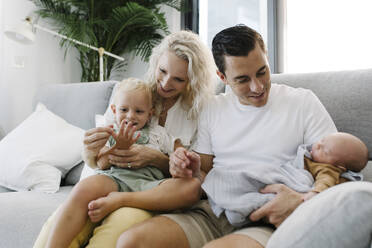 Lächelnde Eltern mit Söhnen, die zu Hause auf dem Sofa sitzen - TYF00258