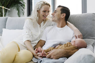 Man carrying baby in arm sitting by woman on sofa at home - TYF00259