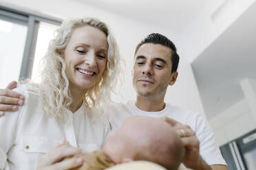 Smiling woman carrying baby sitting by man at home - TYF00261