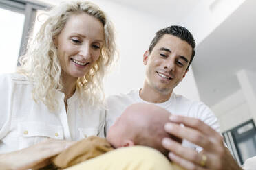 Lächelnde Mutter mit Baby auf dem Schoß, das bei einem Mann zu Hause sitzt - TYF00262