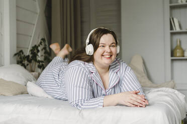 Glückliche Frau, die zu Hause auf dem Bett liegend Musik über drahtlose Kopfhörer hört - SEAF00957