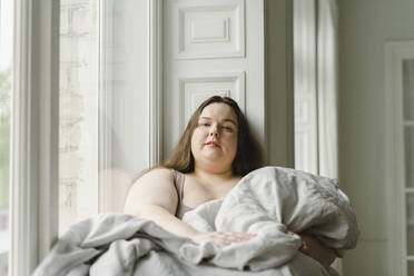 Woman with blanket sitting by window at home - SEAF00966