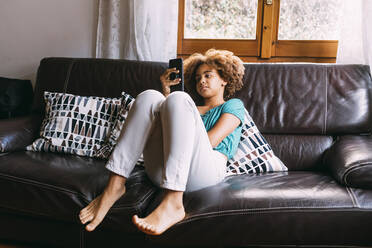 Mädchen mit Handy auf dem Sofa sitzend zu Hause - MEUF06360