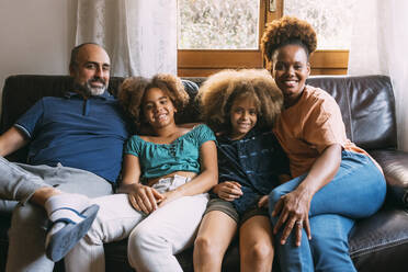 Lächelnder Mann und Frau mit Kindern, die zu Hause auf dem Sofa sitzen - MEUF06365