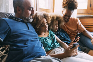 Parents looking at children using smart phones sitting on sofa - MEUF06366