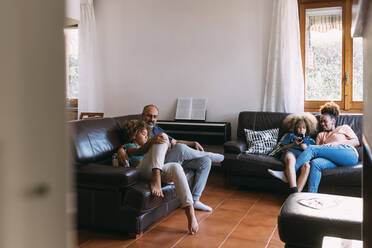 Eltern, die auf dem Sofa im Wohnzimmer sitzend ihre Kinder beim Telefonieren beobachten - MEUF06368