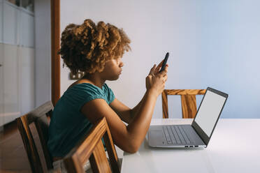 Girl sitting with laptop using smart phone at home - MEUF06378