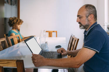 Man using laptop sitting with daughter at table - MEUF06380