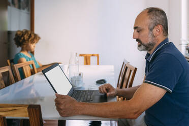 Mann mit Laptop sitzt mit Tochter am Tisch - MEUF06380