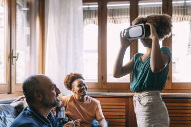 Mädchen trägt Virtual-Reality-Simulator vor der Familie zu Hause - MEUF06389
