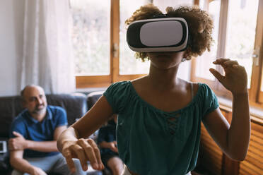 Girl wearing virtual reality simulator in front of father and son at home - MEUF06390