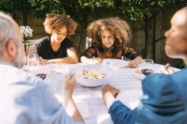 Family having lunch at dining table in backyard - MEUF06402