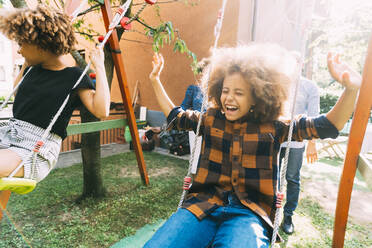 Cheerful boy with sister swinging in backyard - MEUF06408