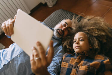 Vater teilt Tablet-PC mit Sohn, der zu Hause auf dem Bett liegt - MEUF06434