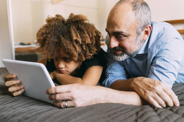 Father sharing tablet PC with boy lying on bed at home - MEUF06436