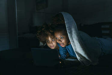 Shocked woman looking at tablet PC with daughter under blanket - MEUF06438