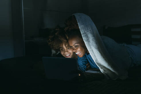 Glückliche Mutter und Tochter teilen sich einen Tablet-PC unter einer Decke zu Hause - MEUF06439
