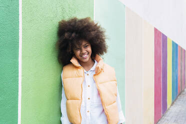 Happy girl leaning on multi colored wall - PNAF04019