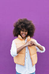 Girl gesturing heart shape against purple background - PNAF04023
