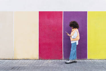 Mädchen benutzt Smartphone an bunter Wand - PNAF04028