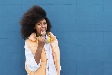 Girl licking lollipop standing in front of blue wall - PNAF04059