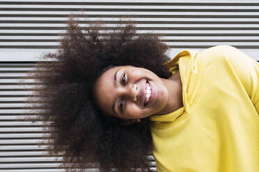 Glückliches Mädchen mit Afrofrisur vor einer Wand stehend - PNAF04065