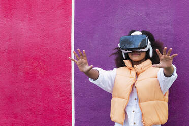 Girl wearing virtual reality simulator gesturing in front of purple and pink wall - PNAF04088