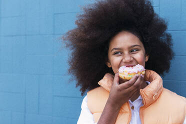 Girl enjoying doughnut in front of blue wall - PNAF04091